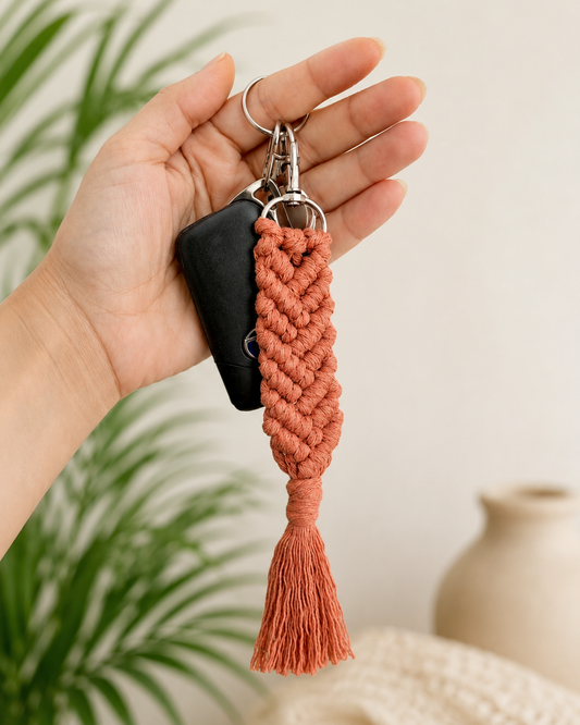 Hand holding a terracotta macrame keychain attached to car keys with tassel detail and boho style.
