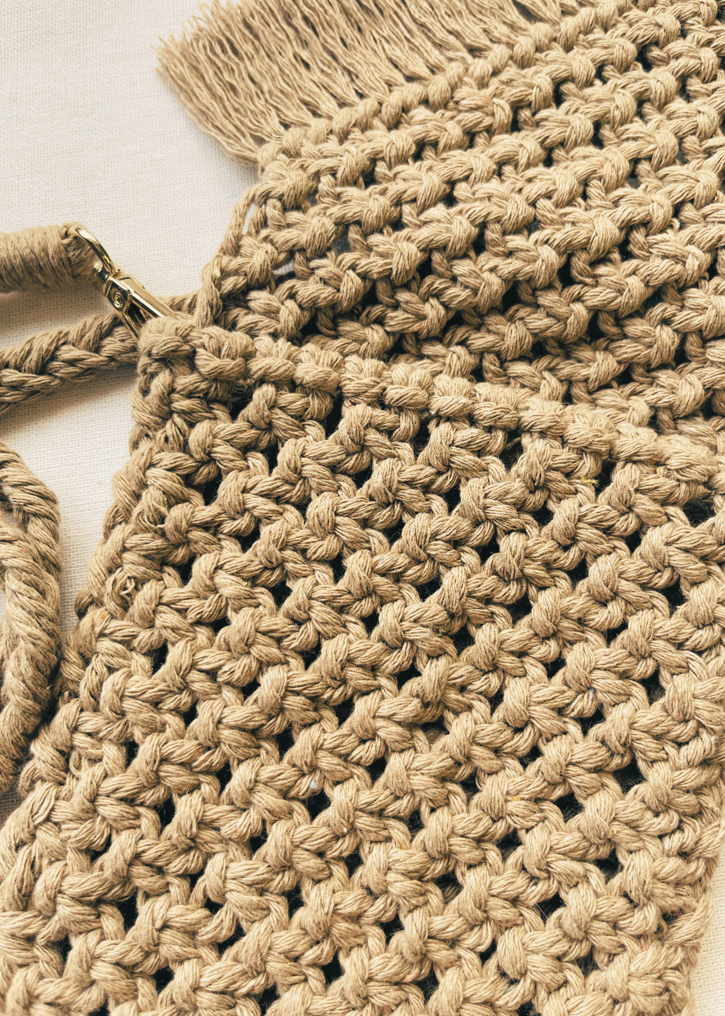 Close-up of a beige macrame bag with tassels on a light background