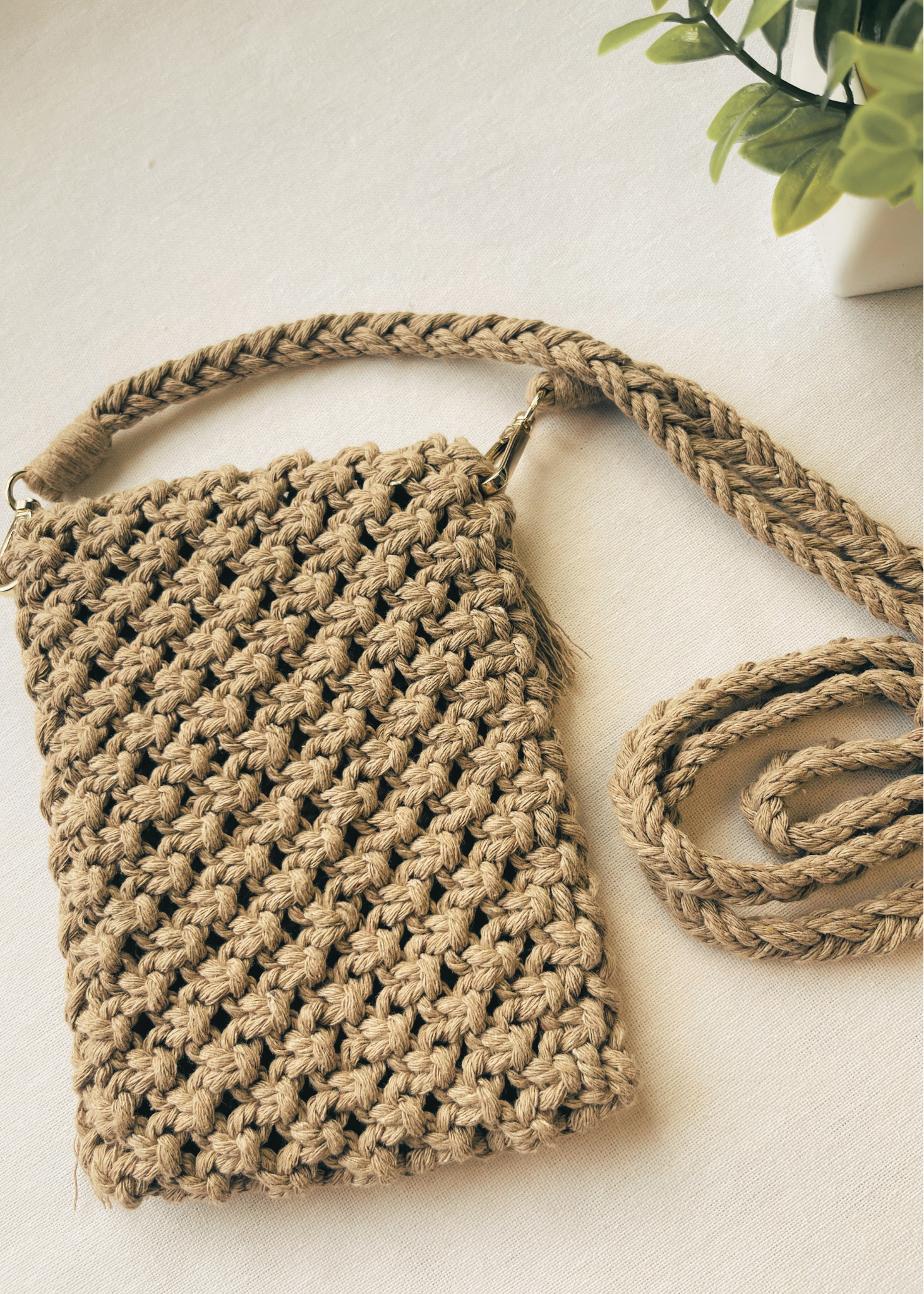 Macrame bag with a strap on a light surface with a plant in the corner