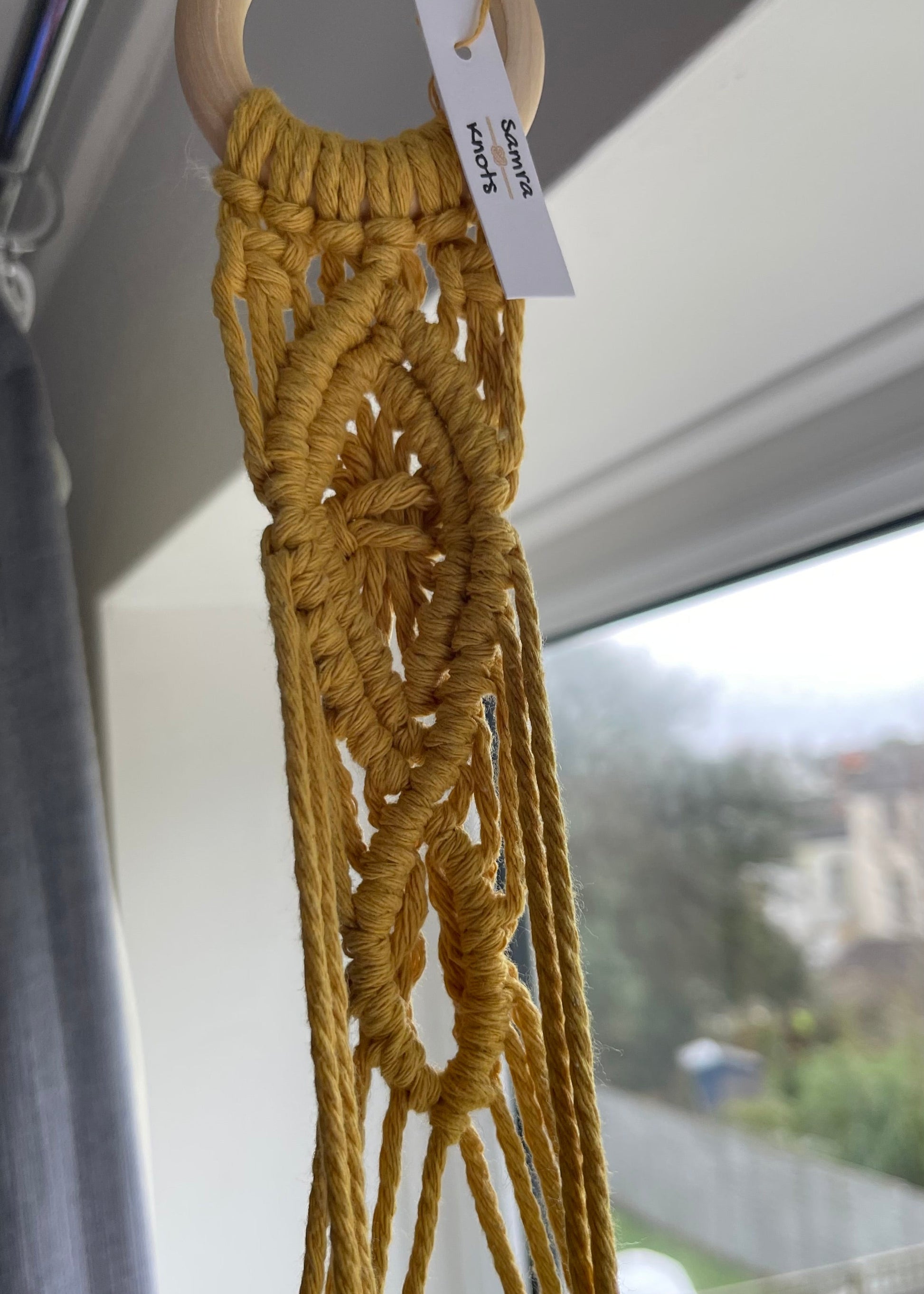 Macrame plant hanger with a tag on a neutral background