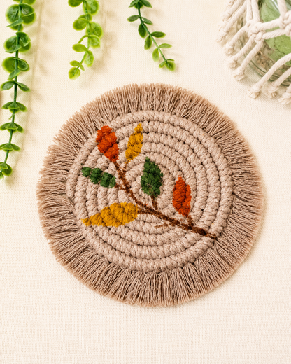 Handmade boho floral macrame coaster with cotton cord, fringe edges and embroidered flower motif in earthy colours.