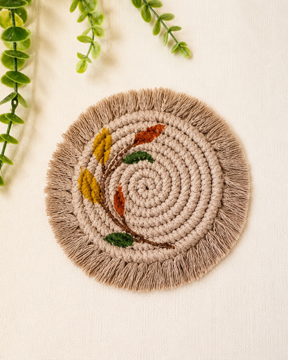 Boho floral macrame coaster handmade from cotton cord with embroidered leaf design and fringe in beige and earthy tones.