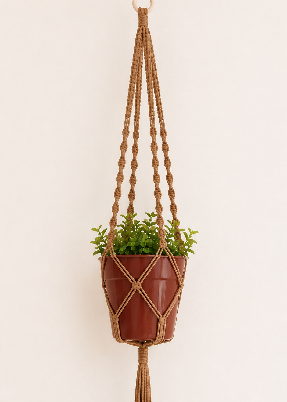 Light brown macrame plant hanger handmade with cotton cord and wooden ring, featuring spiral and square knot details with a terracotta pot on an off-white background.