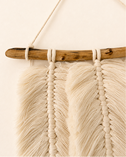Close-up of handmade macrame feathers hanging from a natural wood branch