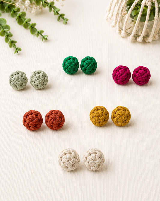 Handmade macramé flower stud earrings in off-white, mustard, terracotta, pink and green displayed on a soft neutral background.