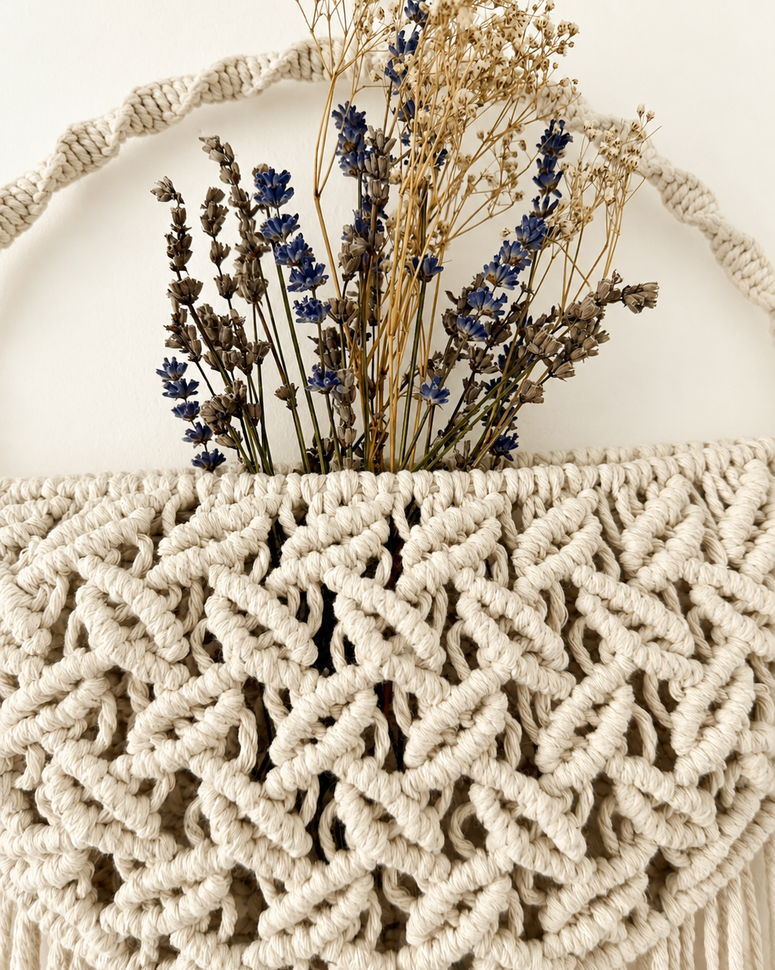 Handmade macrame wall pocket holding dried lavender flowers for boho home decor.