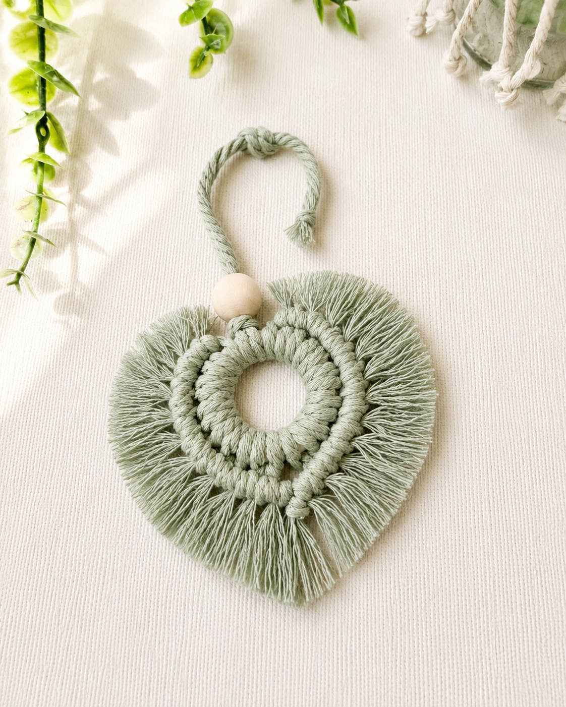 Sage green macrame heart car charm with fringe and wooden bead, handmade boho rear view mirror charm.