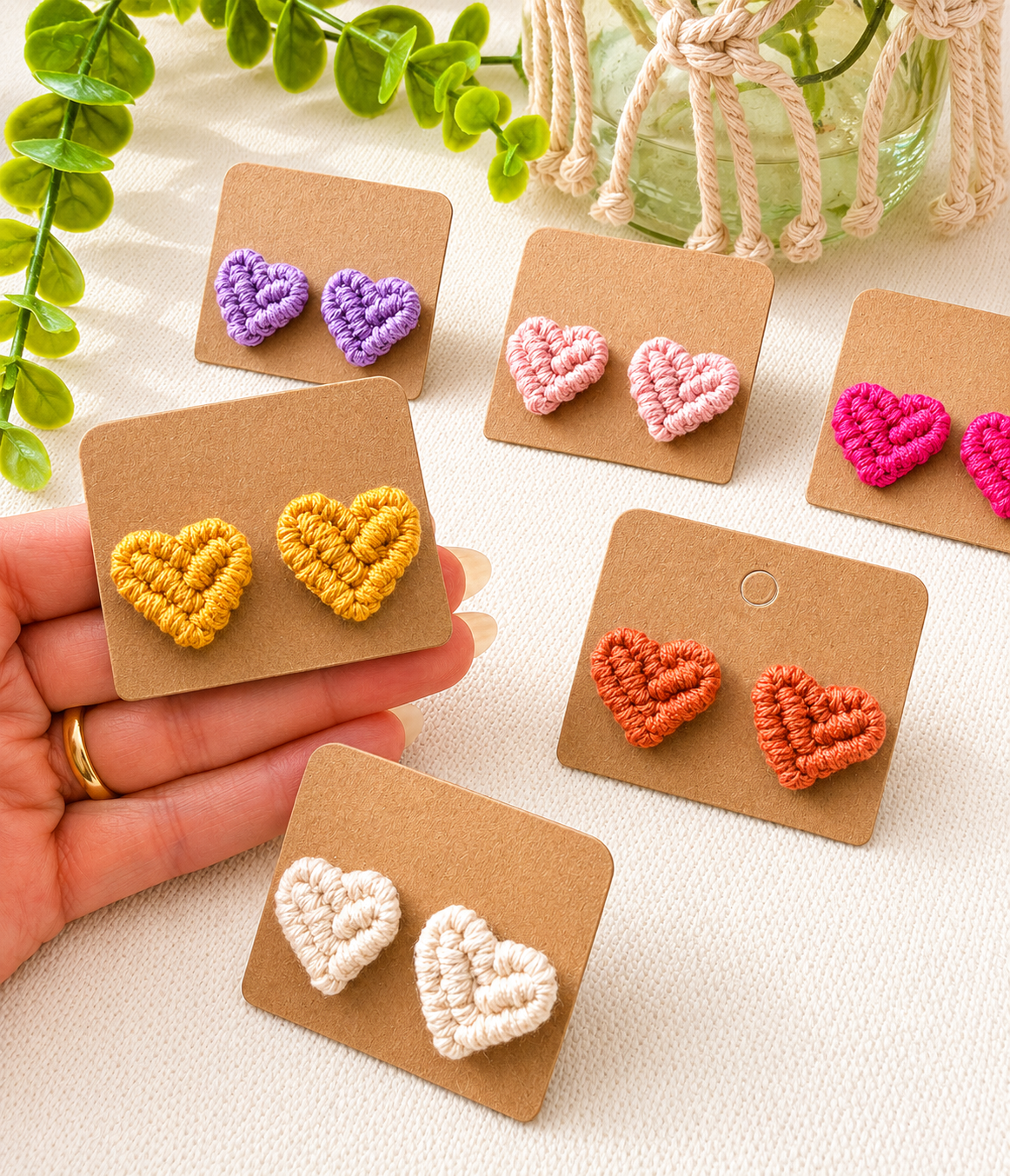 Colorful heart-shaped earrings on brown cards with a hand holding one set.
