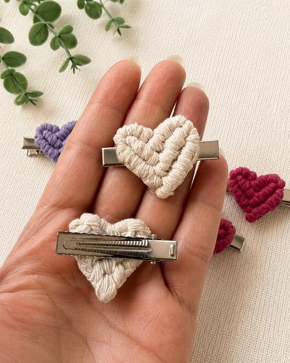 Hand holding a pair of handmade macrame heart hair clips to show their size.