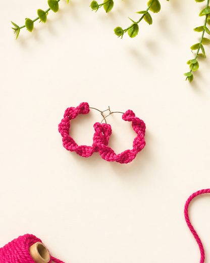 Fuchsia pink handmade macramé hoop earrings on a neutral fabric background
