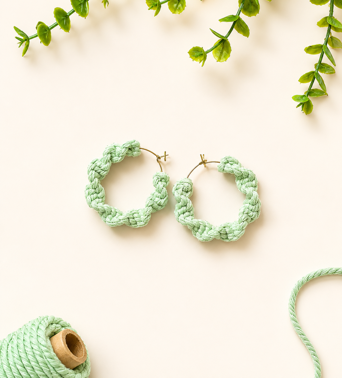 Mint green handmade macramé hoop earrings on a neutral fabric background