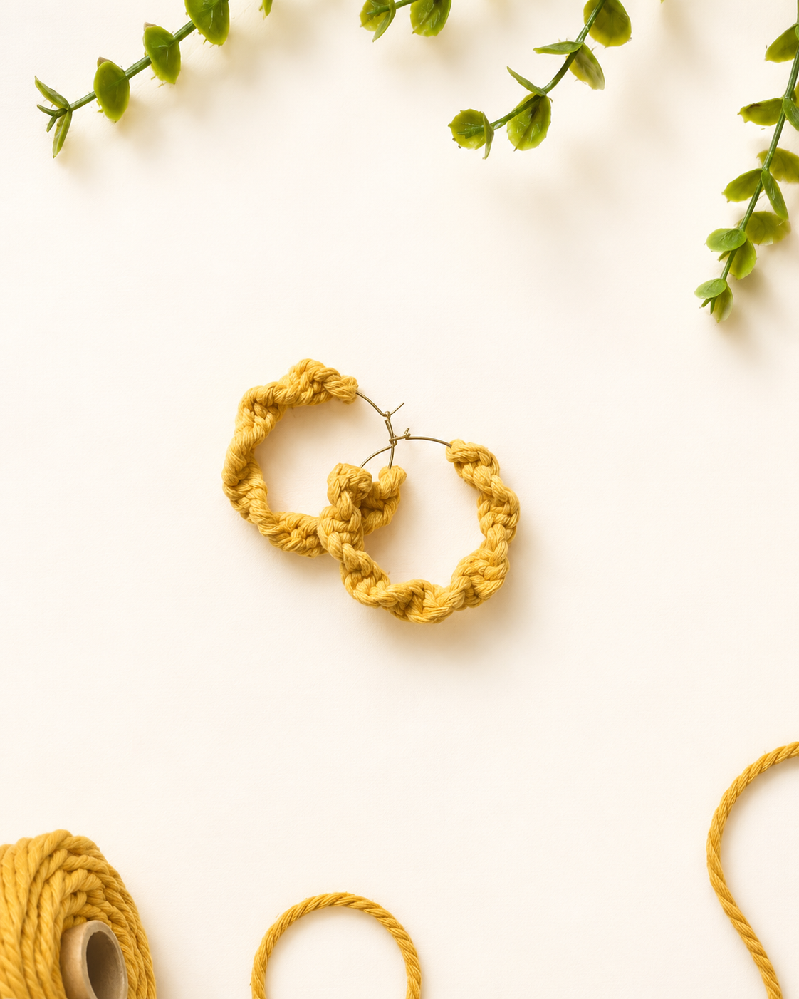 Mustard yellow handmade macramé hoop earrings on a neutral fabric background