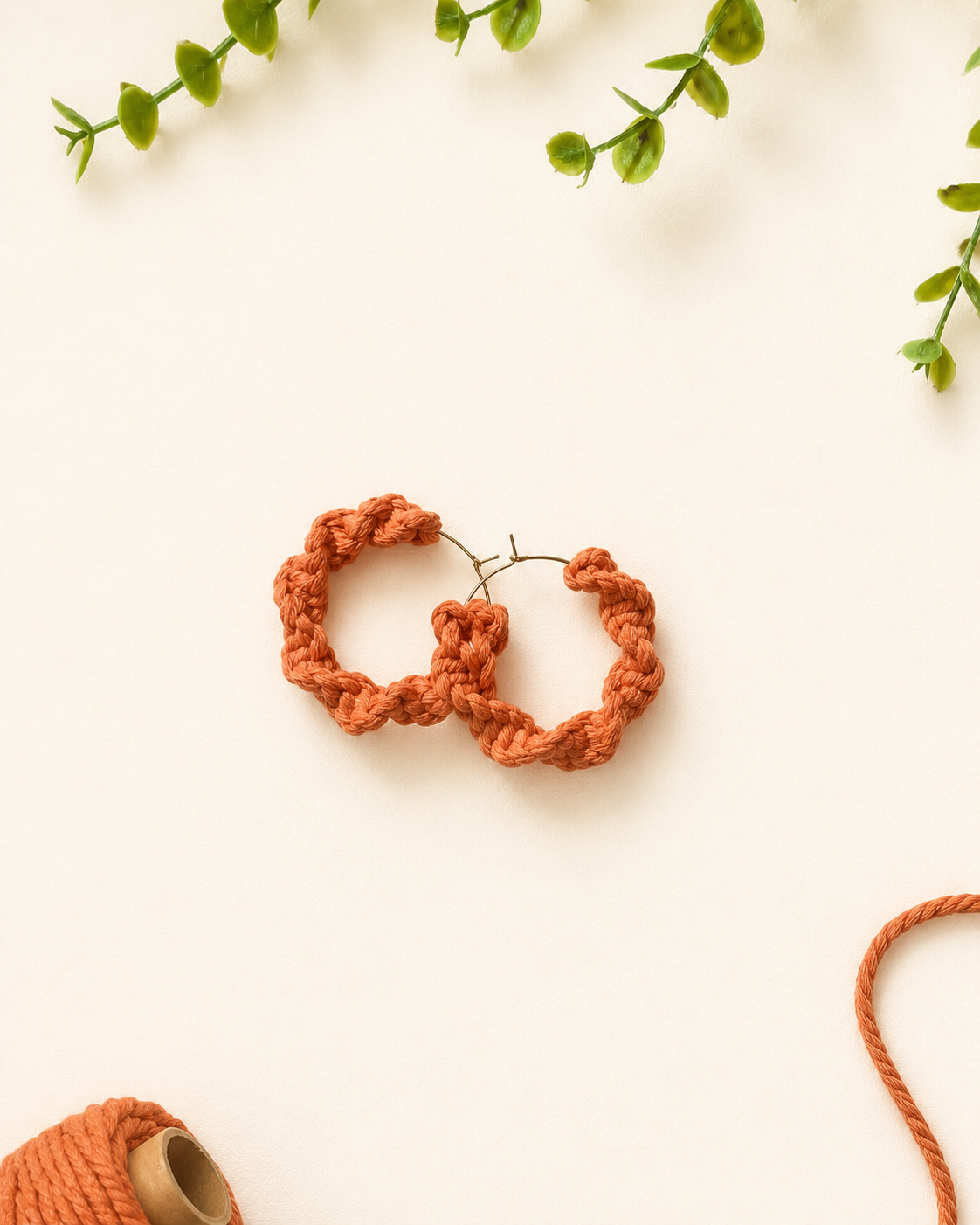 Terracotta handmade macramé hoop earrings on a neutral fabric background