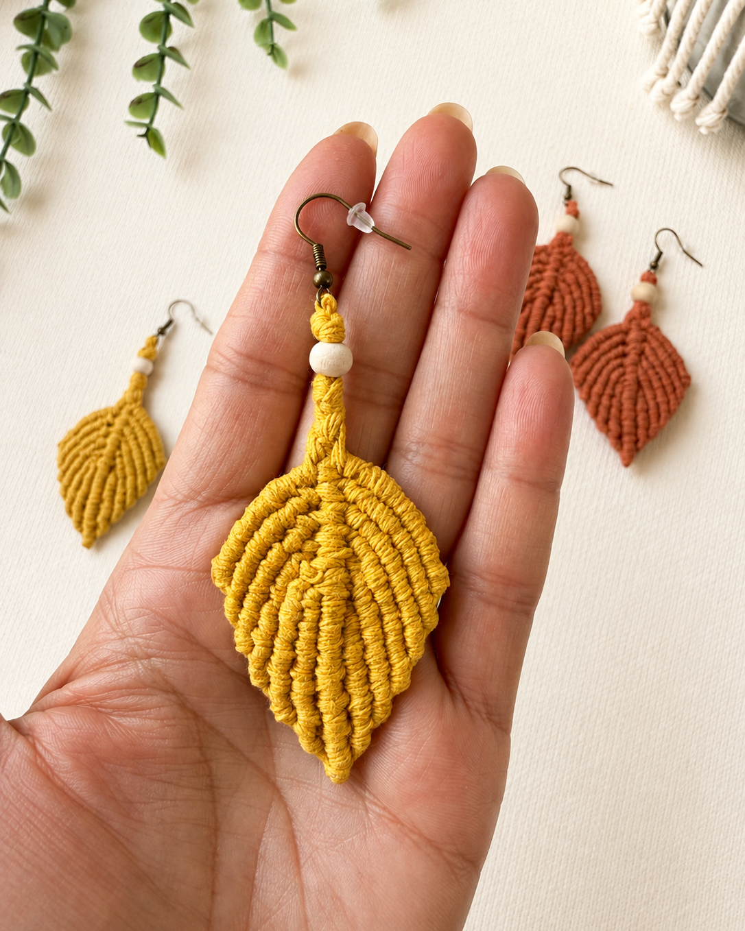 Close-up of a handmade mustard macrame leaf earring held in hand to show its size and intricate knot details.