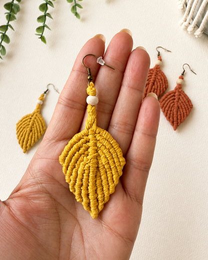 Close-up of a handmade mustard macrame leaf earring held in hand to show its size and intricate knot details.