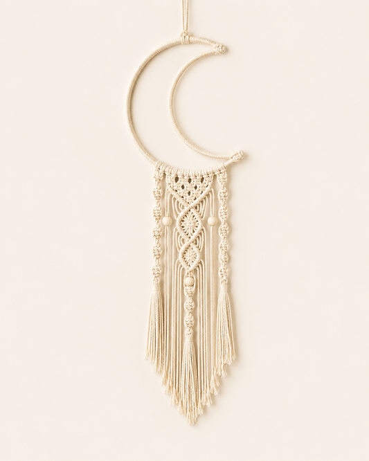Handmade macrame crescent moon wall hanging in natural cotton with decorative knots, wooden beads and tassel fringe on a warm off-white background.