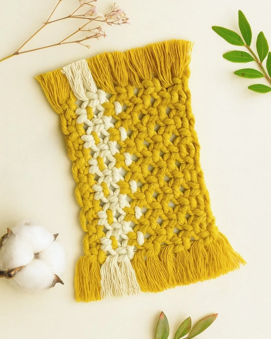 Handmade mustard macramé mugrug with off-white accent stripe, styled with dried flowers and Samra Knots tag on a soft beige background.