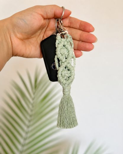 Handmade sage green macrame flower keychain with tassel attached to keys, shown in a lifestyle setting.