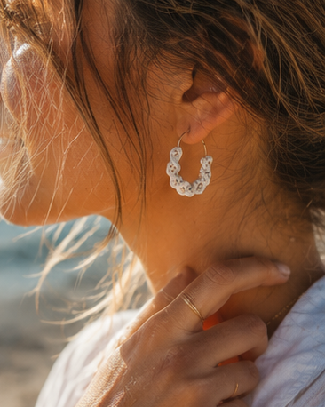 Close-up of a woman wearing handmade off-white spiral macramé hoop earrings at the beach in a boho summer style