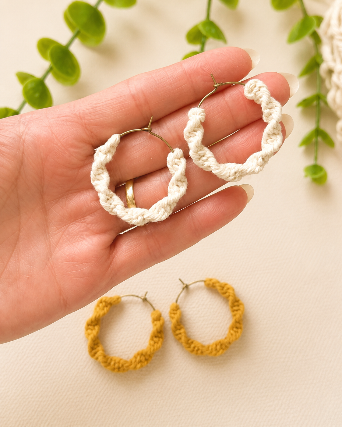 Hand holding off-white macramé spiral hoop earrings showing size and scale.