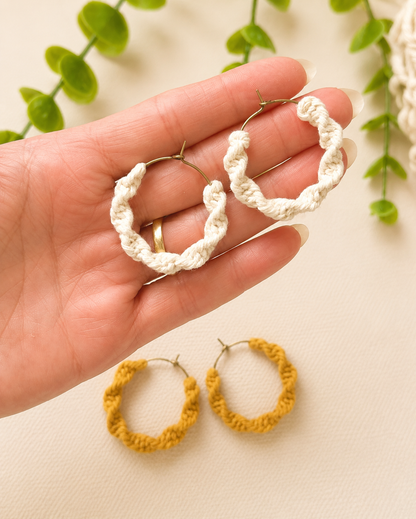 Hand holding off-white macramé spiral hoop earrings showing size and scale.