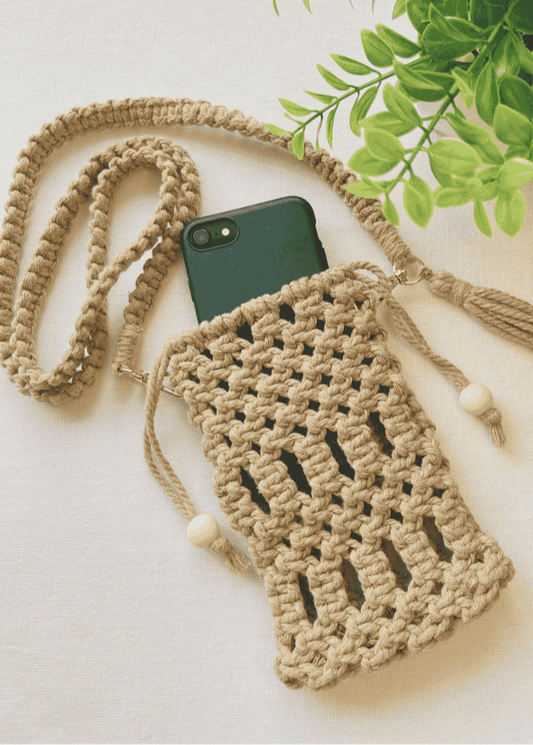Handmade macramé phone bag in light brown cotton cord with phone inside, styled with braided strap and tassels