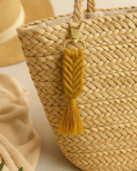 Woven straw bag with a yellow tassel keychain on a neutral background