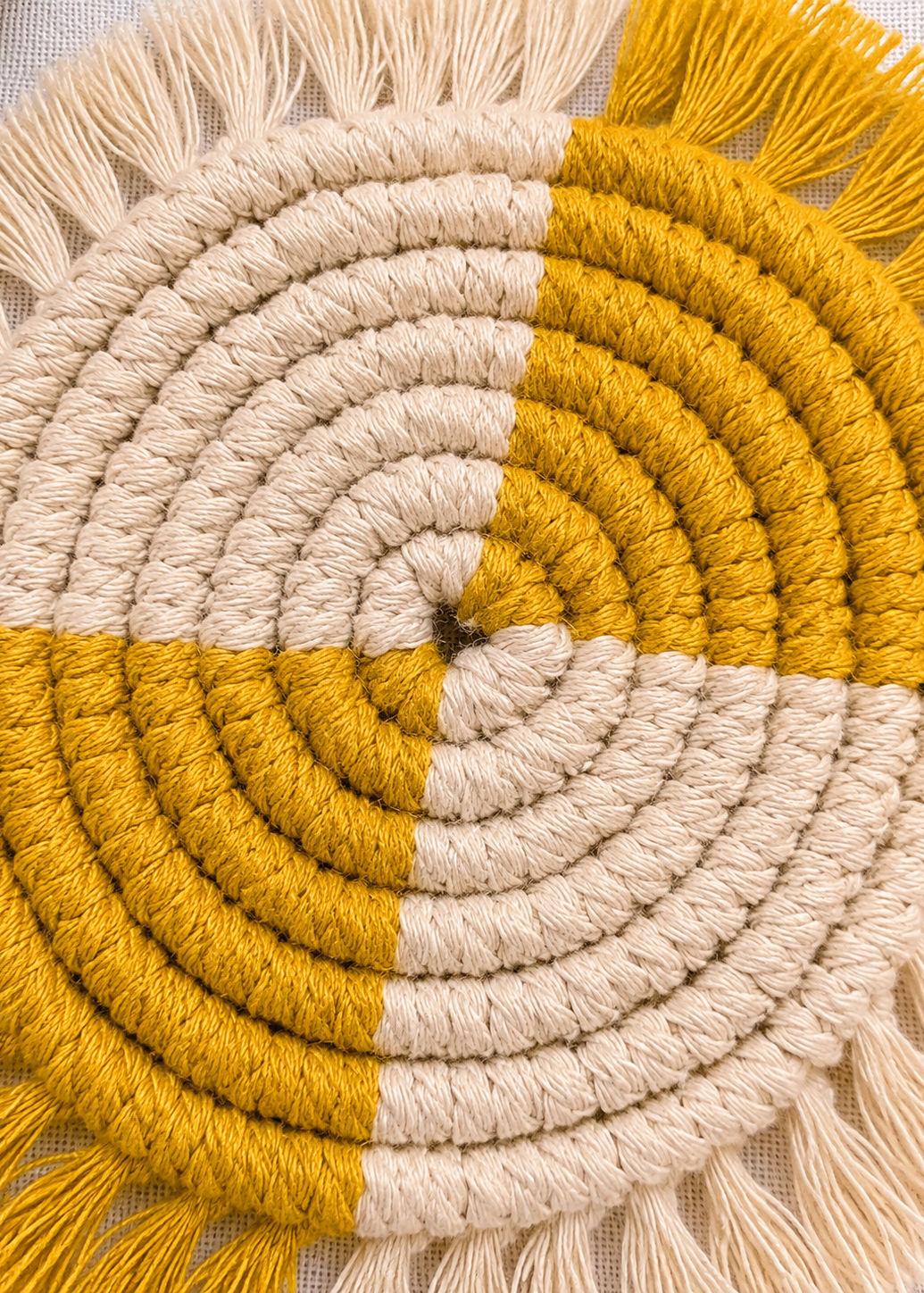 Close-up of a round woven mat with concentric circles in beige, mustard, and white.