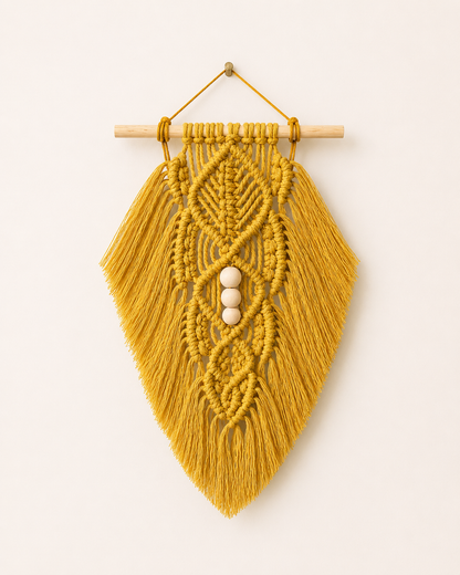 Mustard macrame leaf wall hanging with wooden beads and cotton fringe on an off-white background