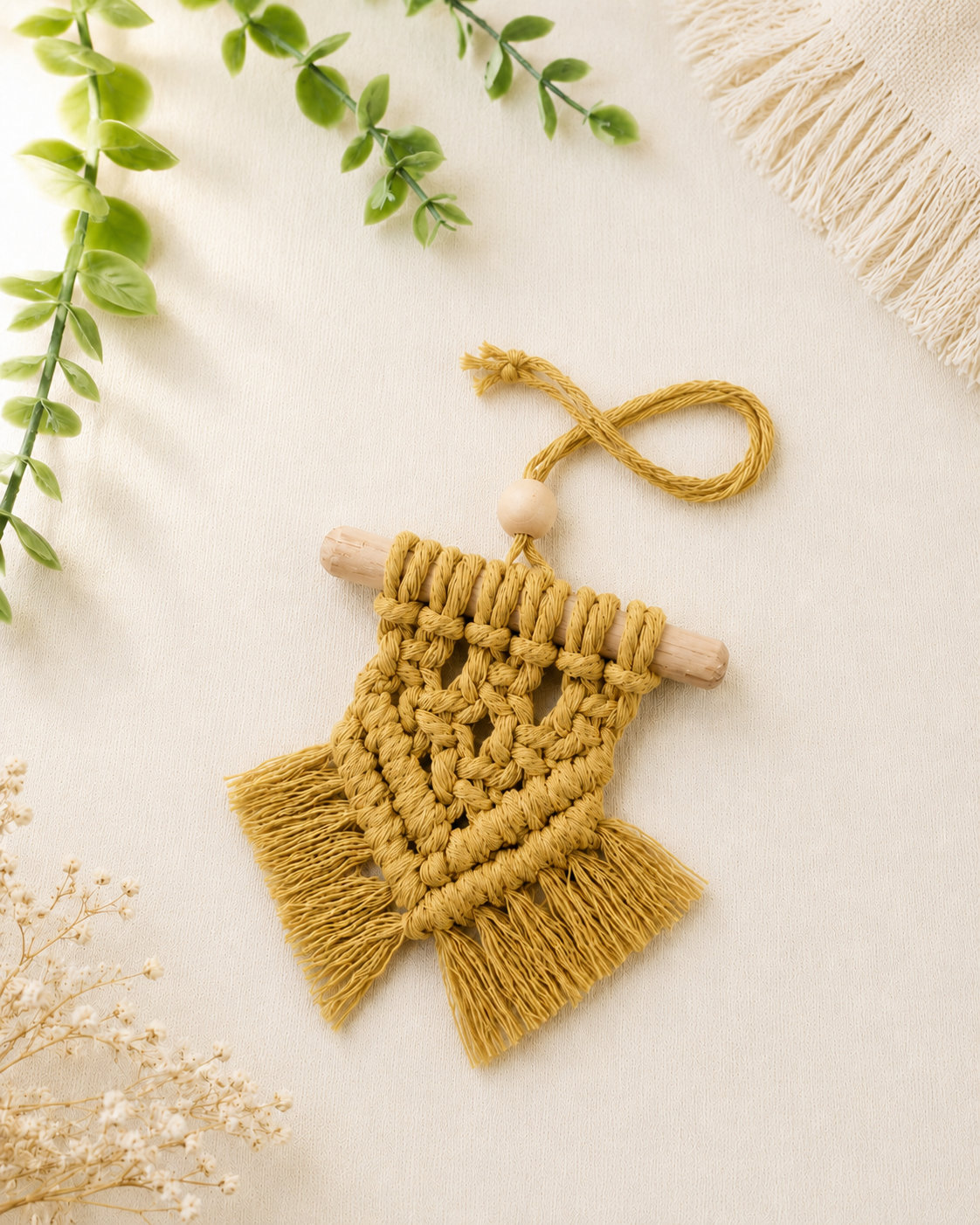 Handmade mustard yellow mini macrame wall hanging with wooden dowel and fringe displayed on an off-white background.