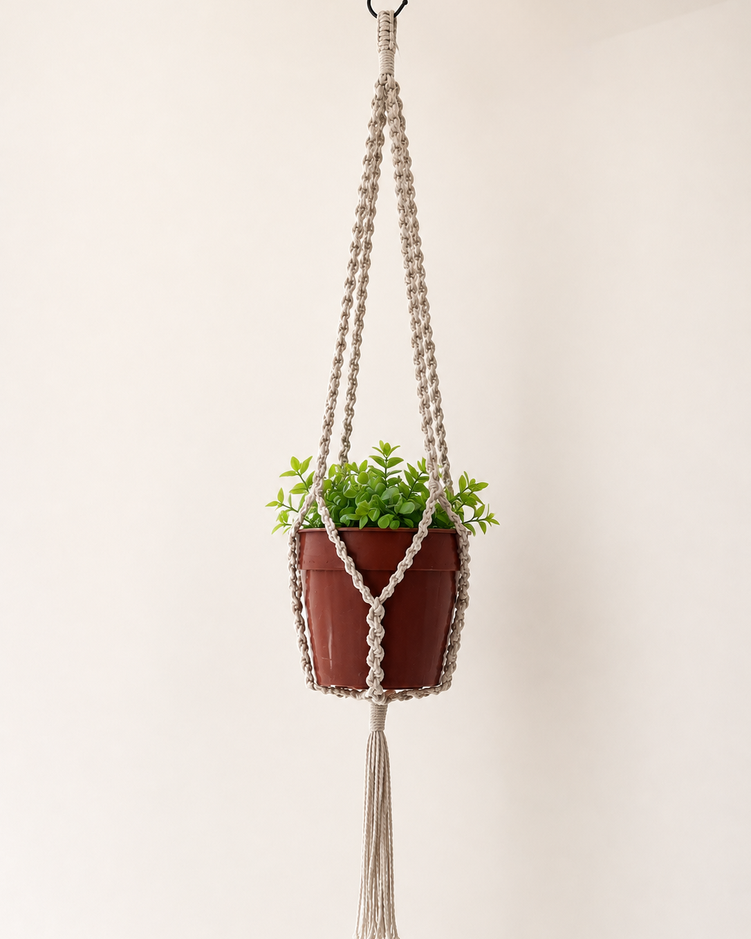 Off-white handmade macrame plant hanger featuring half hitch knots and a tassel, 90 cm long, displayed with a small indoor plant.
