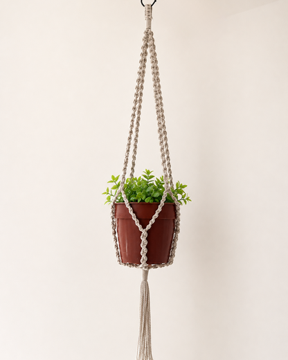 Off-white handmade macrame plant hanger featuring half hitch knots and a tassel, 90 cm long, displayed with a small indoor plant.