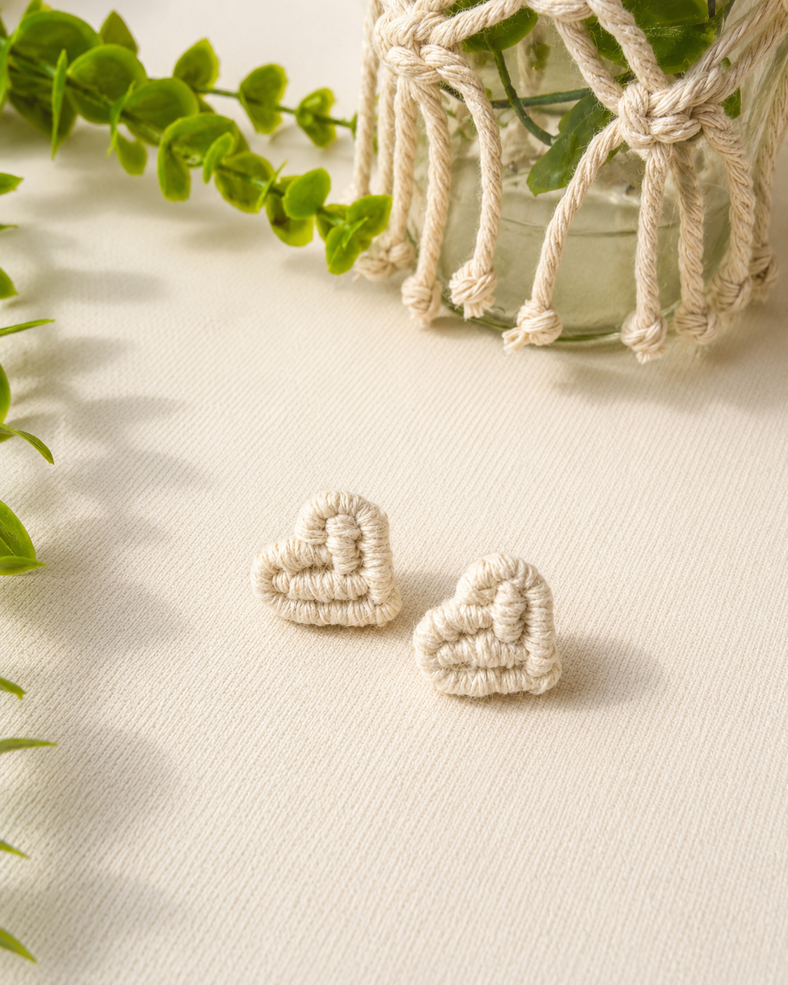 Off-white handmade macramé heart stud earrings on a neutral fabric background