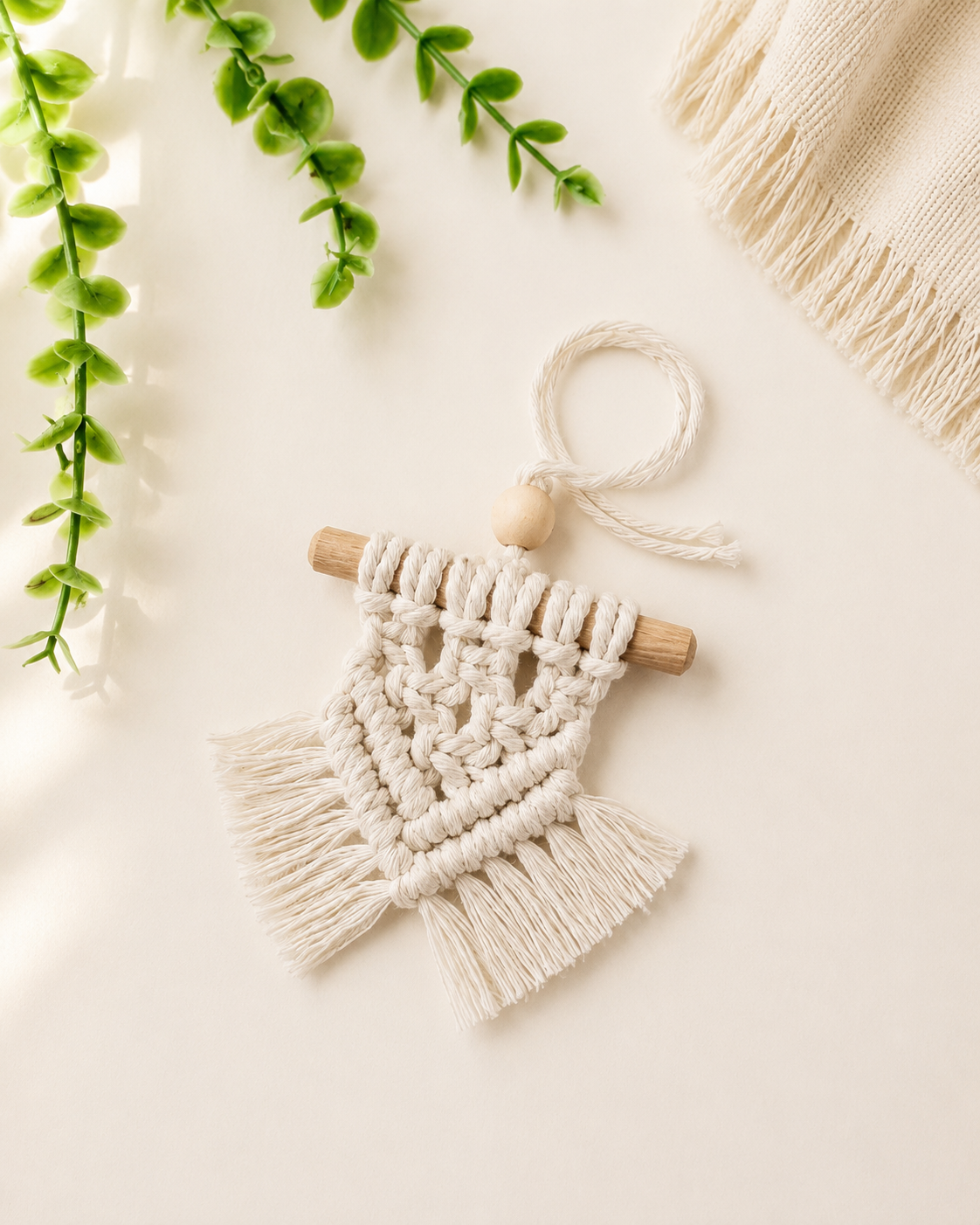Handmade off-white mini macrame wall hanging with wooden dowel and fringe displayed on an off-white background.