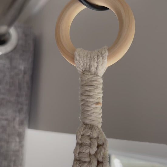 Off-white spiral macrame plant hanger handmade with cotton cord and wooden ring, displayed with a terracotta plant pot in a minimalist boho setting.