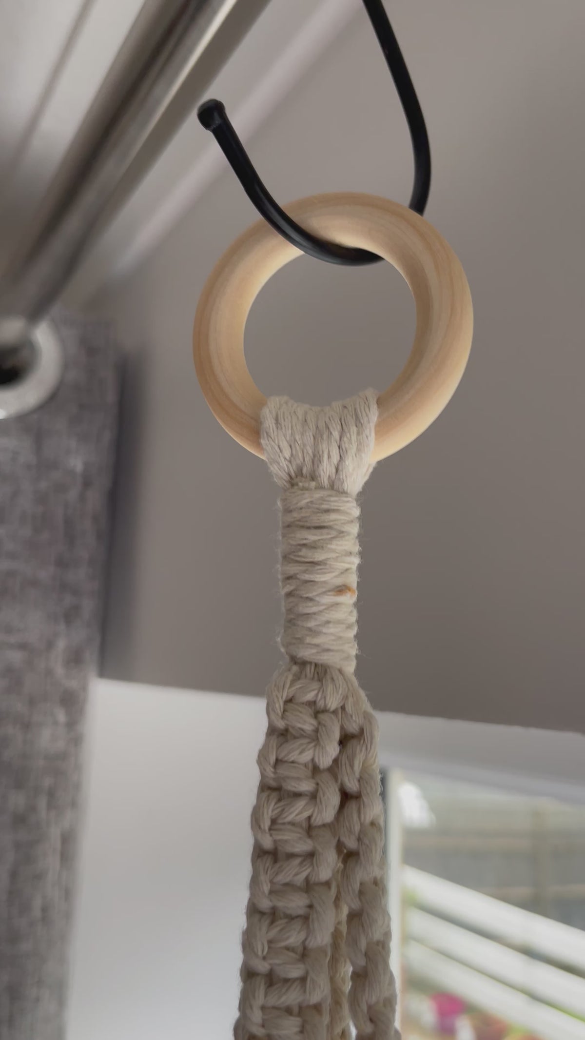 Off-white spiral macrame plant hanger handmade with cotton cord and wooden ring, displayed with a terracotta plant pot in a minimalist boho setting.