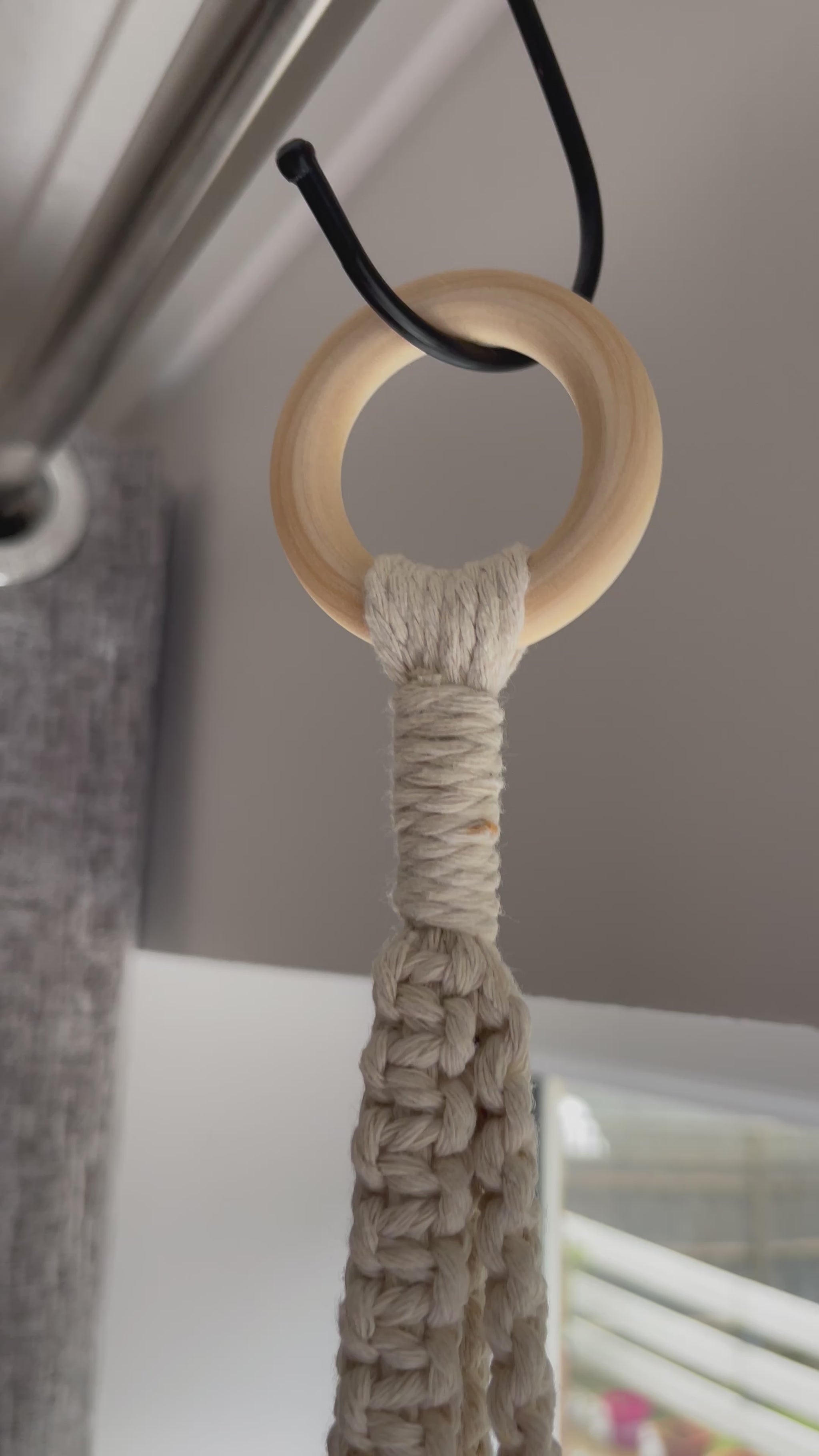 Off-white spiral macrame plant hanger handmade with cotton cord and wooden ring, displayed with a terracotta plant pot in a minimalist boho setting.