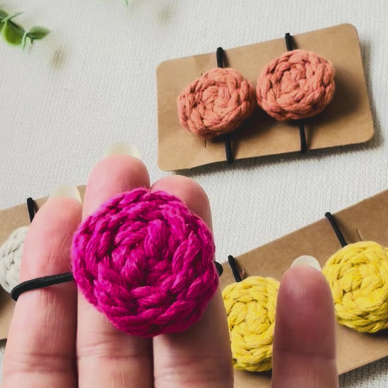 Hand holding a handmade hot pink macrame button hair tie to show its size, texture and everyday design.