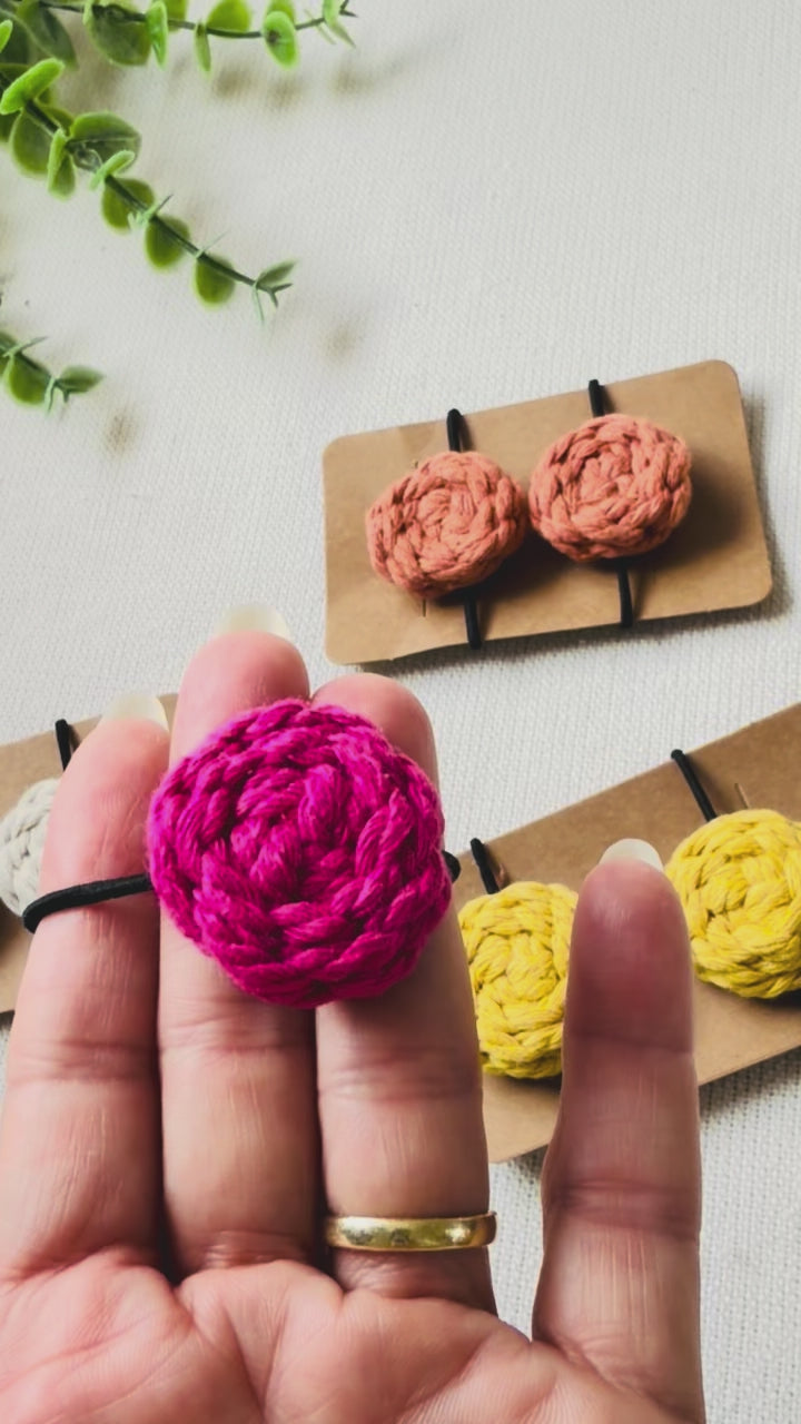 Hand holding a handmade hot pink macrame button hair tie to show its size, texture and everyday design.