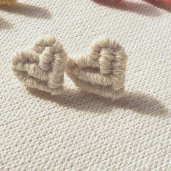 Close-up of off-white handmade macramé heart stud earrings.