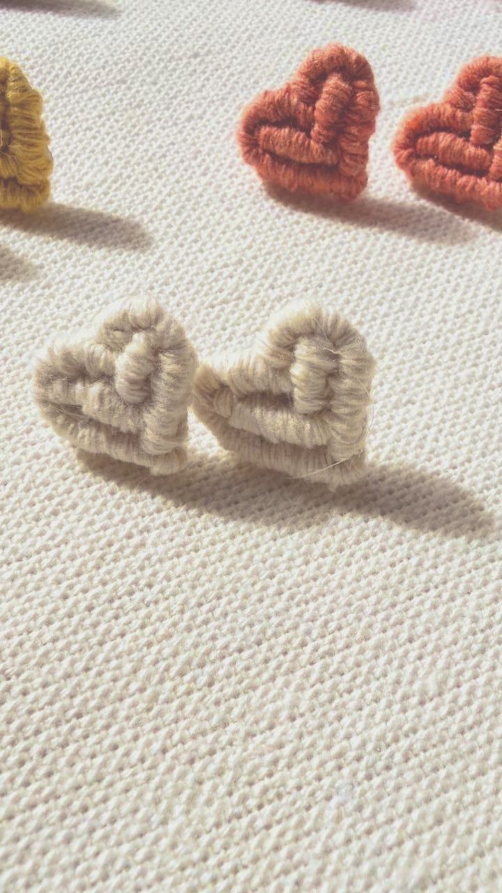 Close-up of off-white handmade macramé heart stud earrings.