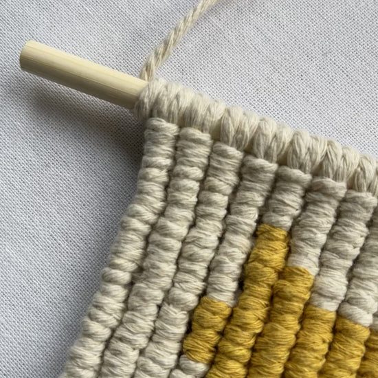Top section of a handmade macrame cat wall hanging attached to a wooden dowel with cotton hanging cord.