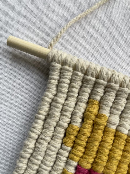 Top section of a handmade macrame cat wall hanging attached to a wooden dowel with cotton hanging cord.