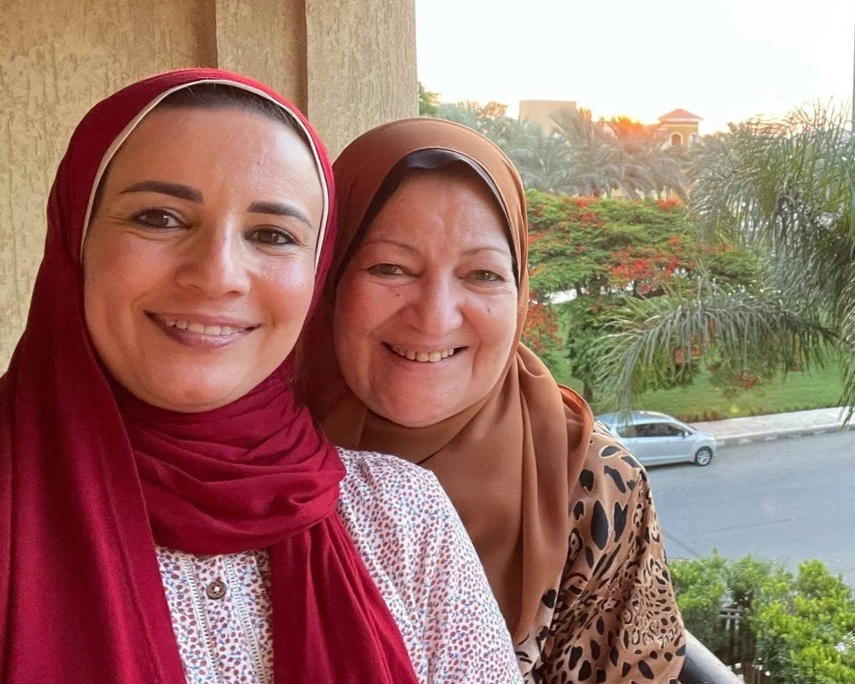 Samra Knots founder smiling with her mother on a sunny balcony, surrounded by greenery and palm trees.