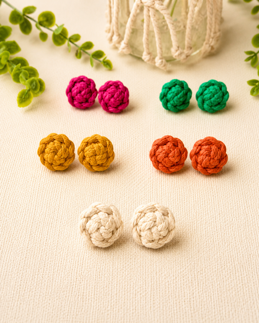 Handmade macramé flower stud earrings in off-white, mustard, terracotta, pink and green displayed on a soft neutral background.