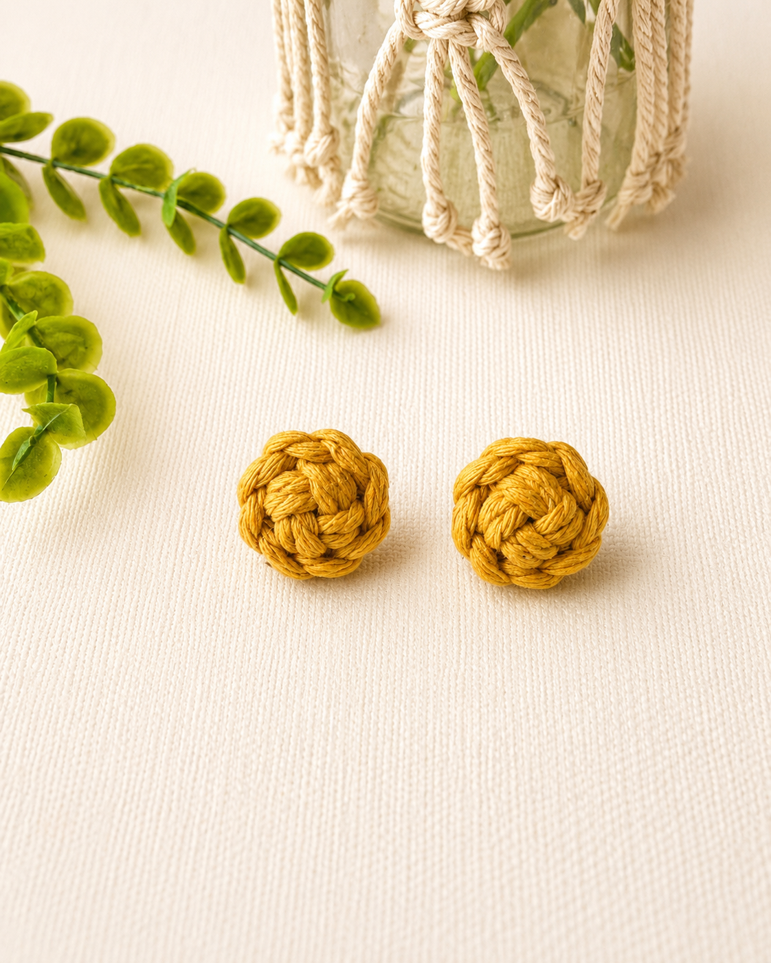 Mustard yellow handmade macramé flower stud earrings on an off-white background.