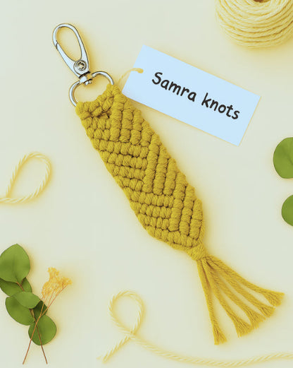 Handcrafted mustard yellow macramé keychain on beige background, styled with eucalyptus and yarn – Samra Knots.