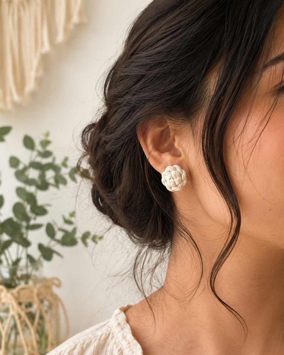 Handmade off-white macramé flower stud earrings worn by a woman in a natural boho lifestyle setting.