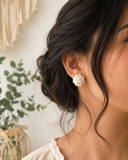 Handmade off-white macramé flower stud earrings worn by a woman in a natural boho lifestyle setting.