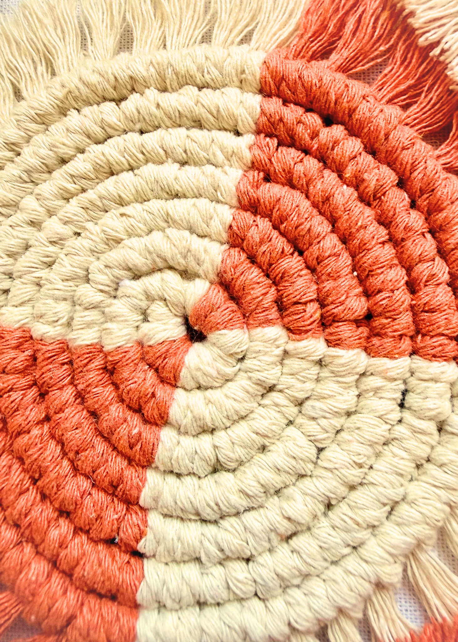 Close-up detail of a handmade terracotta and off white macramé coaster showing soft cotton knots and fringe texture.
